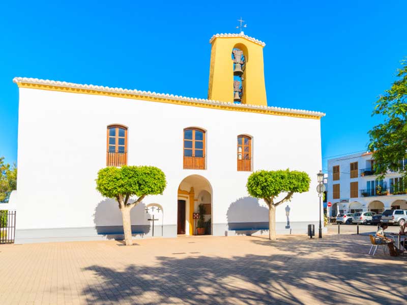 hvid facade og gul farvetårn i kirken i Santa Gertrudis by på øen Ibiza, Spanien.