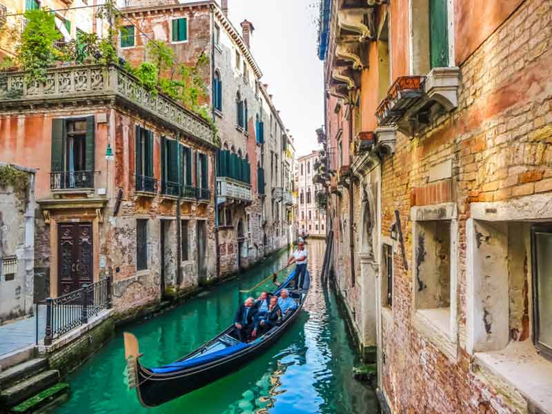 Traditionelle gondoler på en smal kanal mellem farverige historiske huse i Venedig, Italien